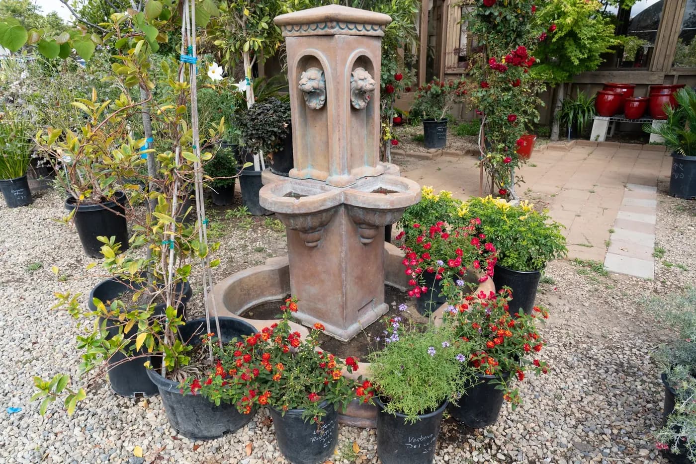 A tall stone garden fountain surrounded by flowering nursery stock