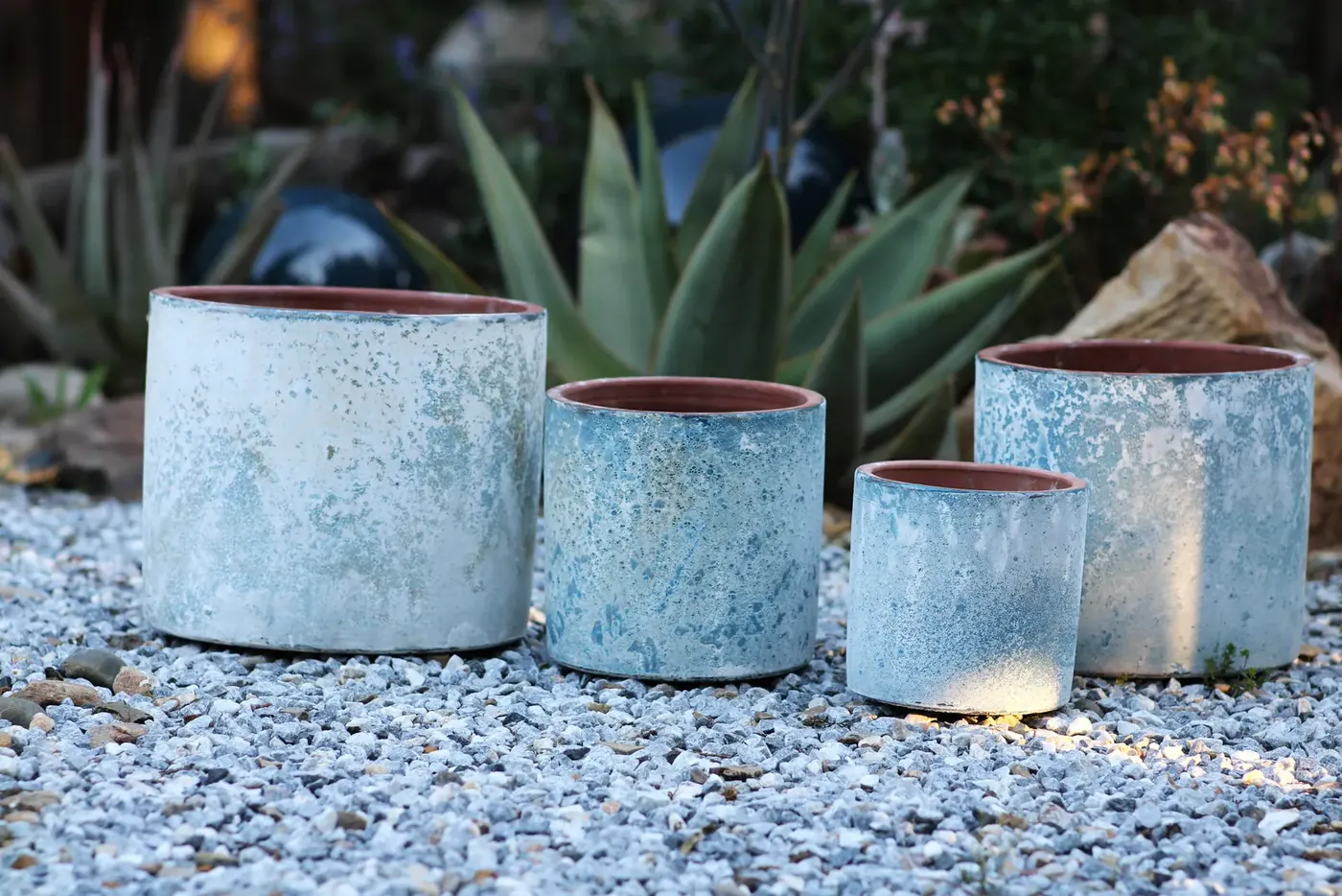Pale blue glazed pots with dark rims arranged on gravel