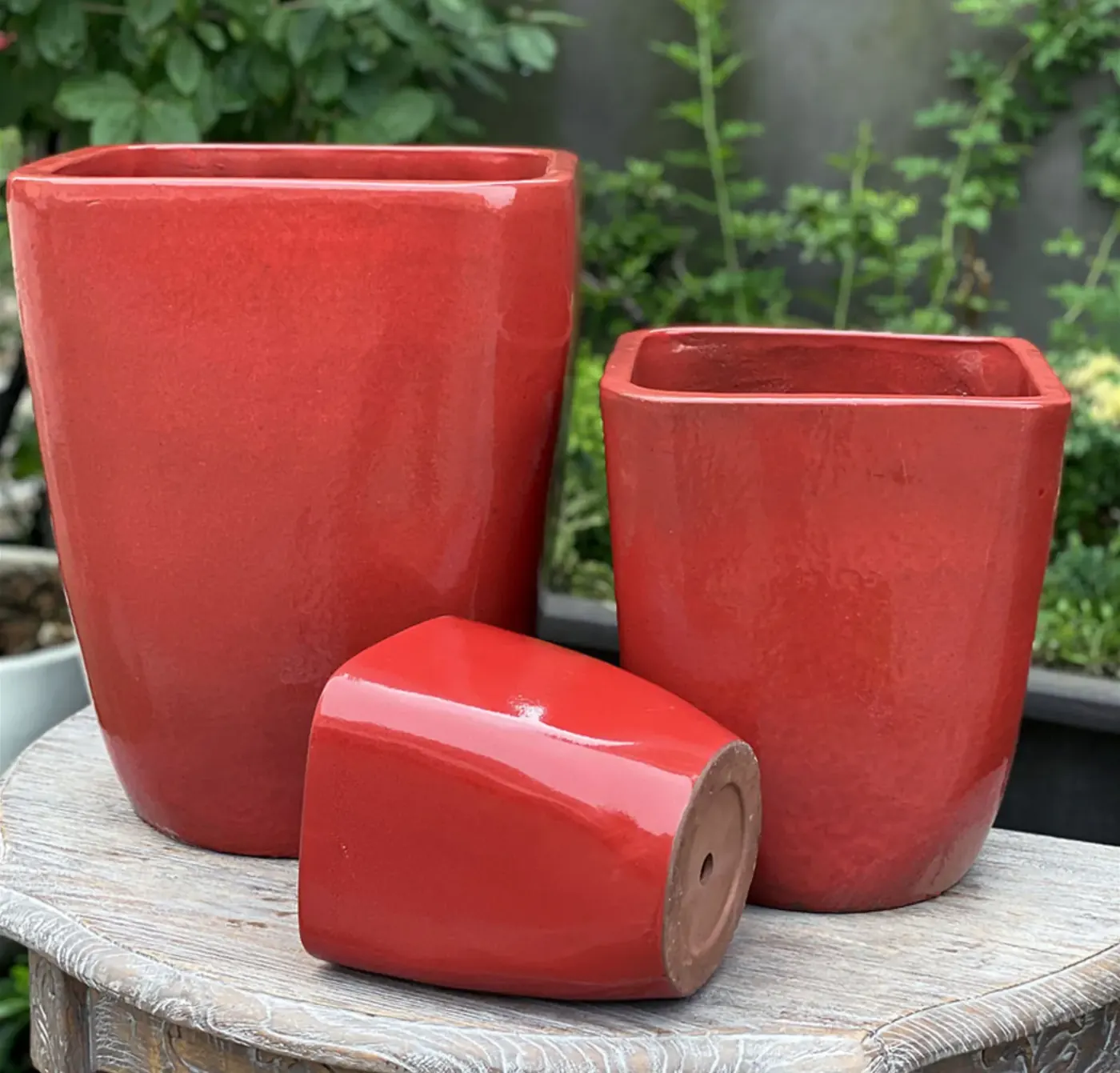 Three glossy red glazed ceramic pots grouped on a stone surface