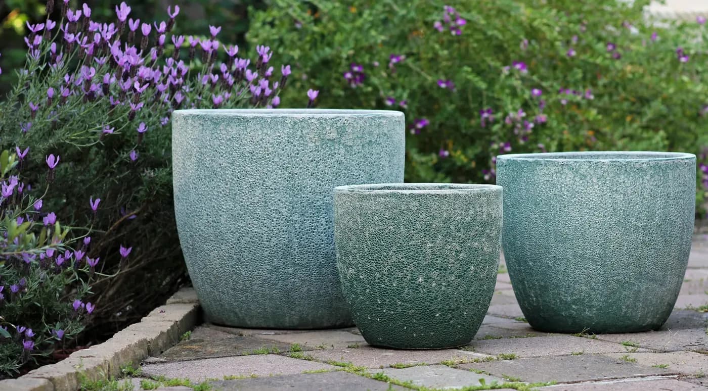 Three speckled teal glazed pots in graduated sizes on a patio