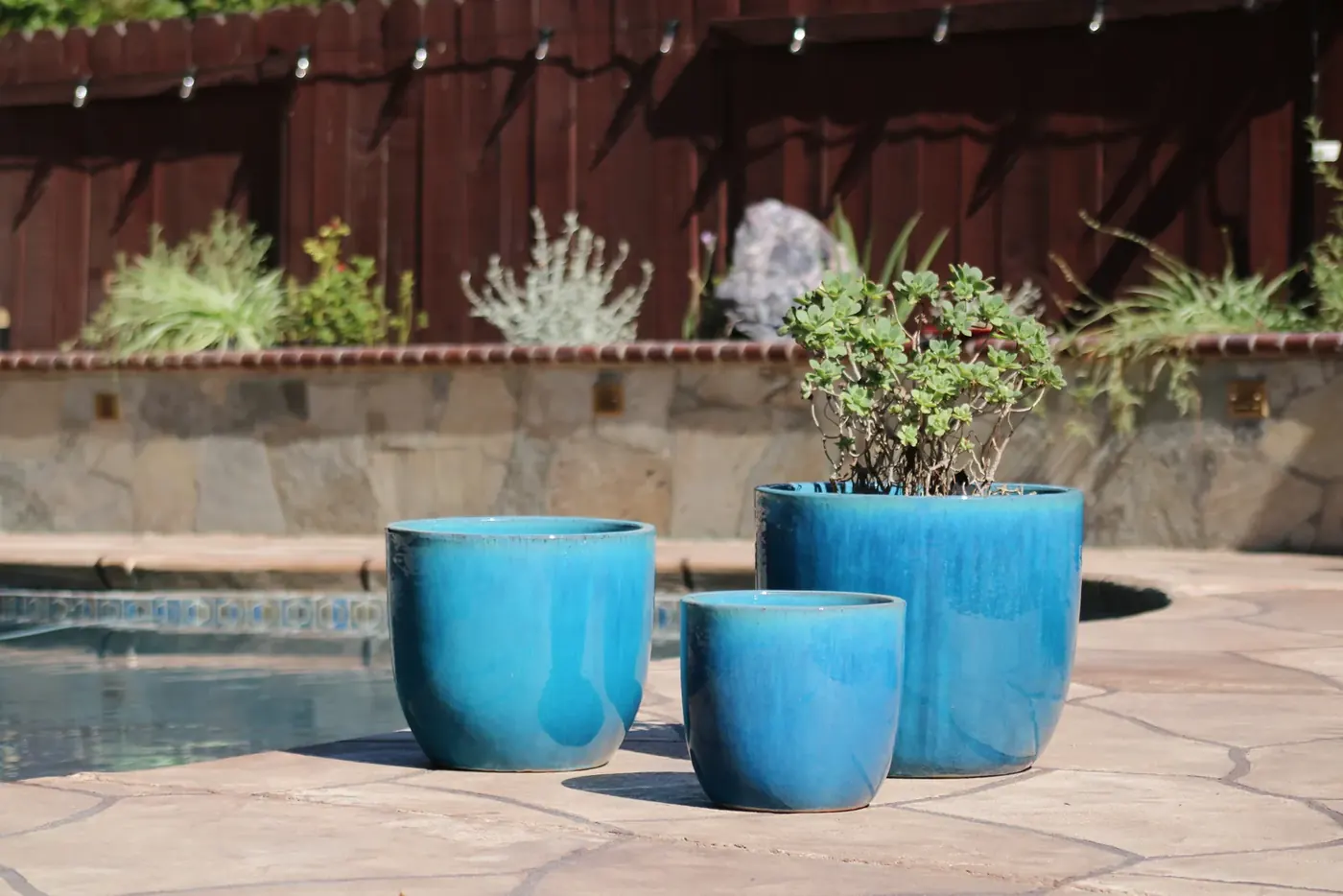 Turquoise glazed pots in three sizes beside a swimming pool